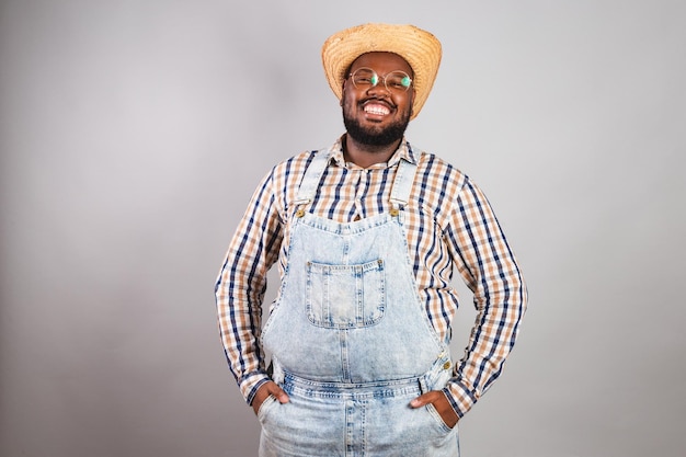 Hombre negro brasileño vestido con ropa de campo de festa junina festa de sao joao con un sombrero de paja con las manos sonrientes en el bolsillo