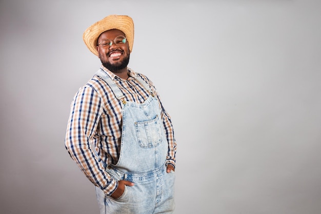 Hombre negro brasileño vestido con ropa de campo de festa junina festa de sao joao con un sombrero de paja con las manos sonrientes en el bolsillo