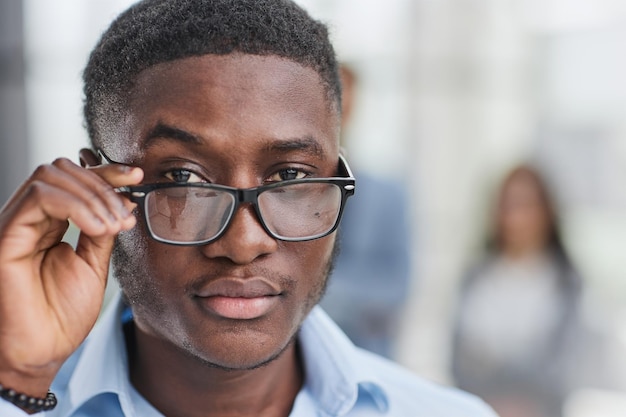 Un hombre negro con una camisa azul se ajusta las gafas.