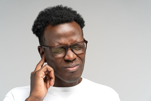 Hombre negro con el ceño fruncido que sufre de tinnitus dolor de oído palpitante cansado de ruido tocando el oído doloroso