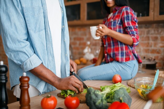 Foto hombre negro cocinando en la cocina, esposa bebe café