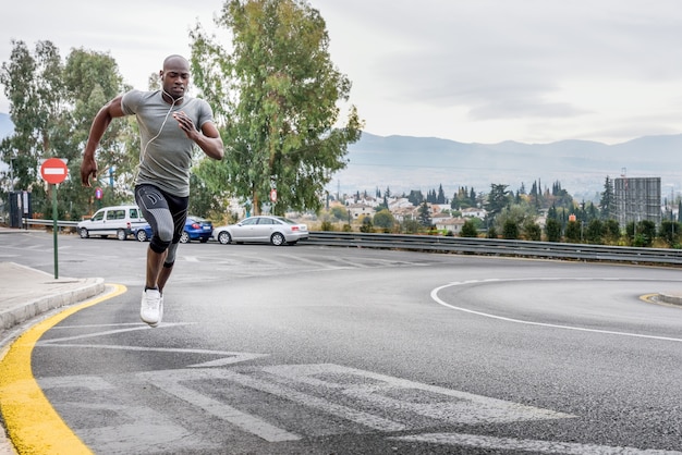 Hombre negro corriendo al aire libre en el camino urbano.