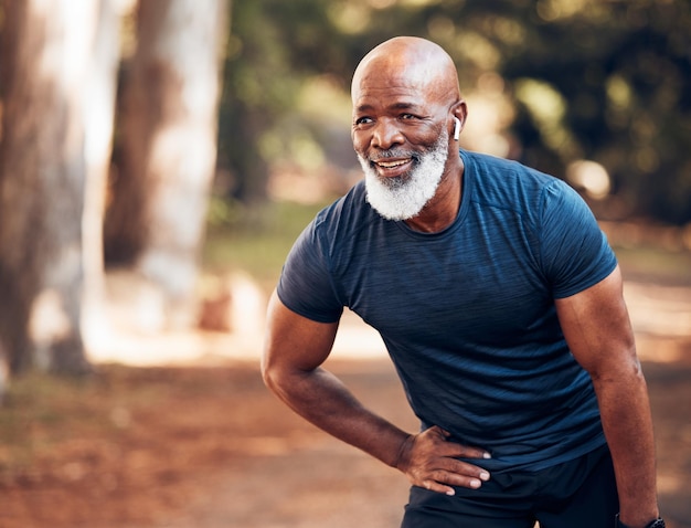 El hombre negro deja de correr y se relaja con vitalidad física y corredor de cardio senior en el parque. Ejercita auriculares y escucha música para motivarte cansado de resistencia y salud al aire libre.