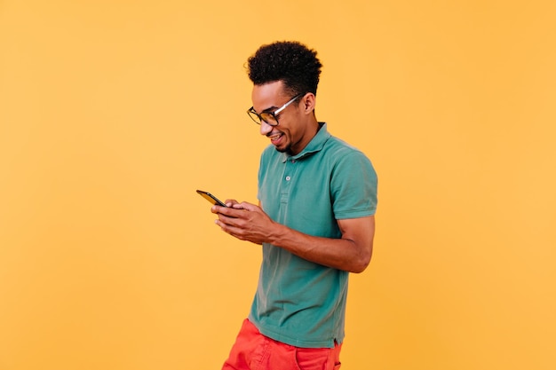 Hombre negro deportivo mirando la pantalla del teléfono y sonriendo Retrato de un tipo alegre con un mensaje de texto de camiseta verde