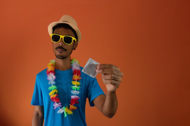 Hombre negro disfrazado para el carnaval de brasil sosteniendo un condón aislado de fondo naranja. Hombre africano en varias poses y expresiones.