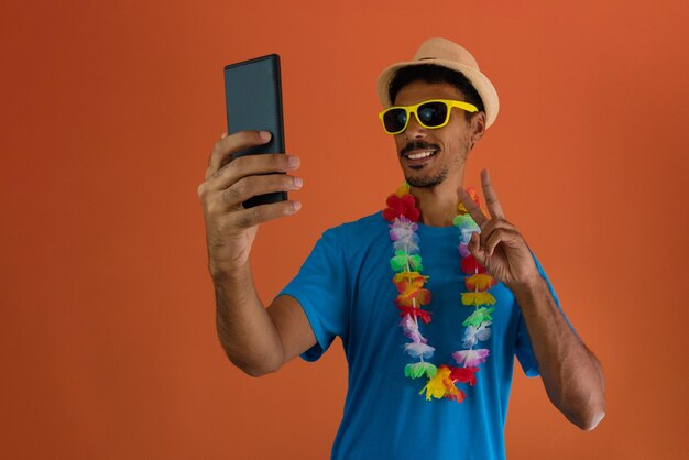 Hombre negro disfrazado para el carnaval de brasil sosteniendo un móvil aislado en un fondo naranja. Hombre africano en varias poses y expresiones.