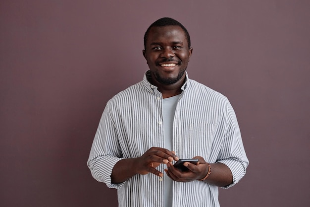 Hombre negro con emoción sincera de pie contra el púrpura y sosteniendo el teléfono inteligente