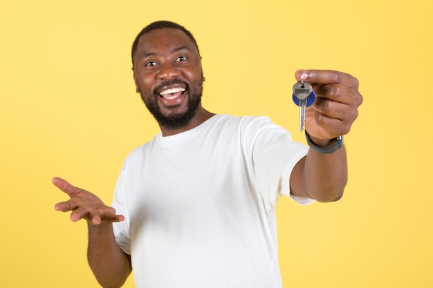 Hombre negro emocionado mostrando llaves comprando casa sobre fondo amarillo