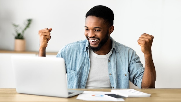 Hombre negro eufórico celebrando el éxito empresarial con los brazos levantados