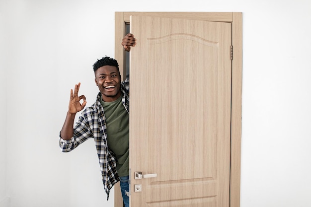 Hombre negro feliz abriendo la puerta gesticulando bien aprobando el nuevo hogar