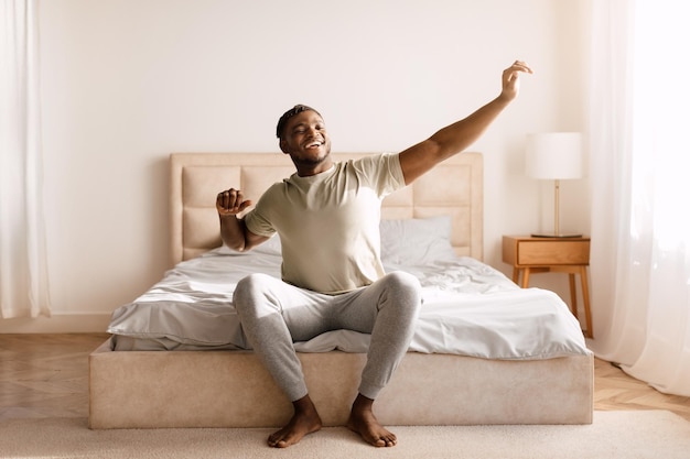 Hombre negro feliz despertando y estirando los brazos en el dormitorio