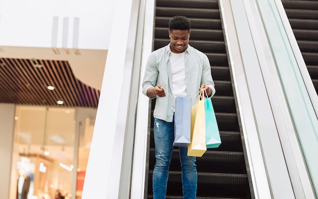 Hombre negro feliz sosteniendo bolsas de compras mirando dentro