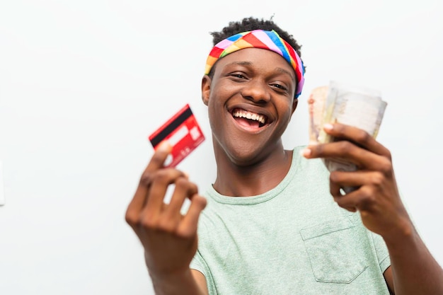 Hombre negro feliz sosteniendo dinero y tarjeta de débito aislado sobre fondo blanco.