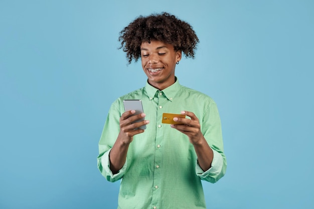 Hombre negro feliz con teléfono celular y compras con tarjeta de crédito o banca en línea usando una nueva aplicación móvil