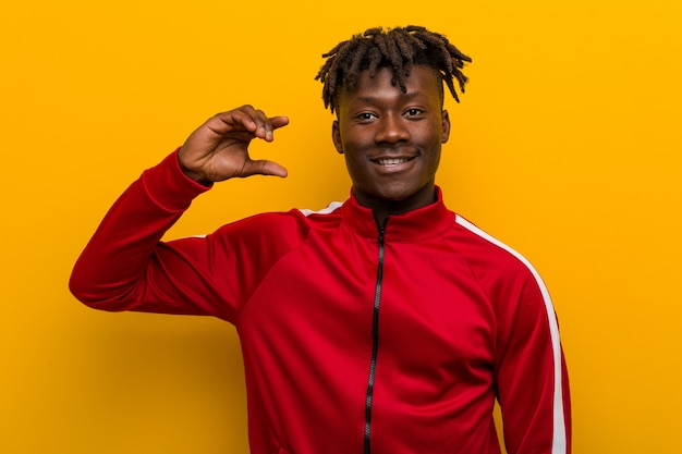 Hombre negro de fitness joven sosteniendo algo poco con los dedos índices, sonriente y confiado.