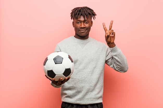 Hombre negro fitness joven sosteniendo una pelota de fútbol que muestra el número dos con los dedos.