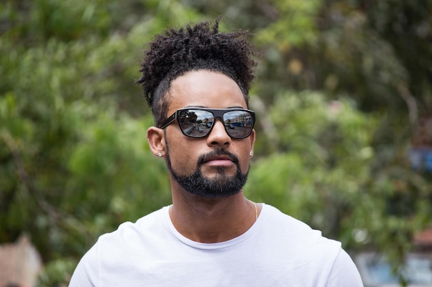 Hombre negro con gafas de sol detrás de árboles verdes