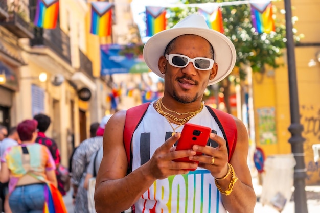 Un hombre negro gay en la fiesta del orgullo escribiendo un mensaje con la bandera LGBT del teléfono