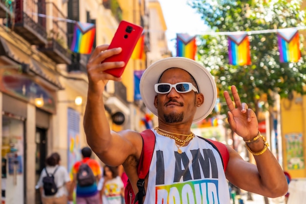 Un hombre negro gay en la fiesta del orgullo haciéndose un selfie con la bandera LGBT del teléfono