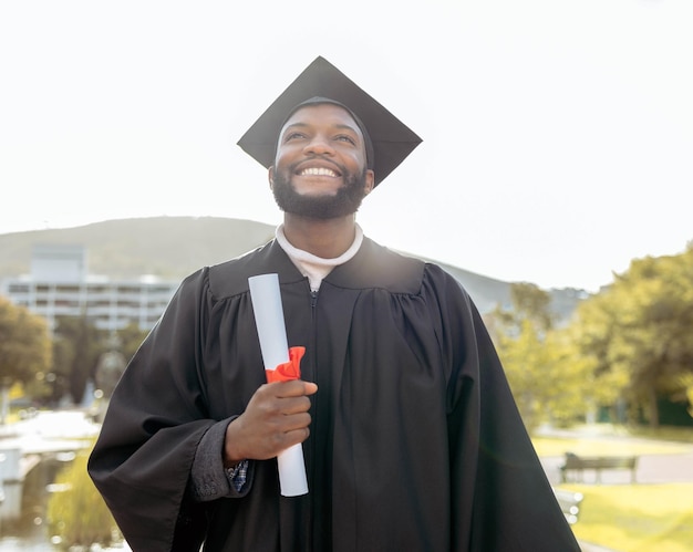 Hombre negro de graduación y pensando en el éxito y las metas en el evento universitario al aire libre Premio de educación de posgrado y sonrisa para un sueño futuro feliz y motivación de aprender esperanza y orgullo