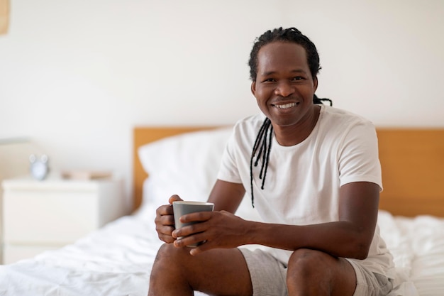Hombre negro guapo descansando en la cama con una taza de café en las manos