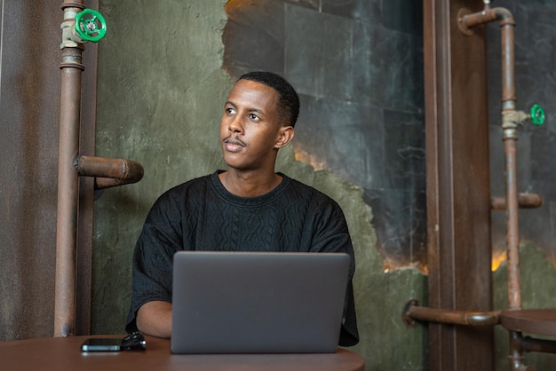 Hombre negro guapo sentado y usando una computadora portátil en el interior