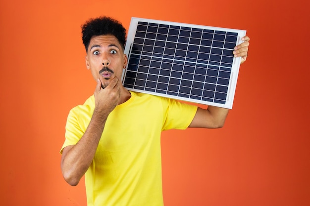 Hombre negro guapo sosteniendo una alcancía y un panel solar aislado en naranja Hombre en una camisa amarilla aislada