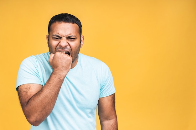 Hombre negro indio afroamericano loco enojado enfurecido furioso con mueca de mal humor en su rostro, con la boca abierta en grito, listo para discutir y jurar, mostrar fuerza, aislado sobre fondo amarillo.