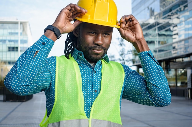 hombre negro ingeniero al final del día al aire libre de pie terminando el trabajo quitándose el casco