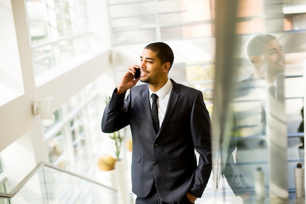 Hombre negro joven hermoso con el teléfono móvil en la oficina
