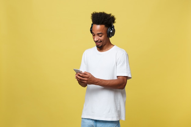 Hombre negro joven que escucha la música sobre sus auriculares. Aislado sobre fondo amarillo.