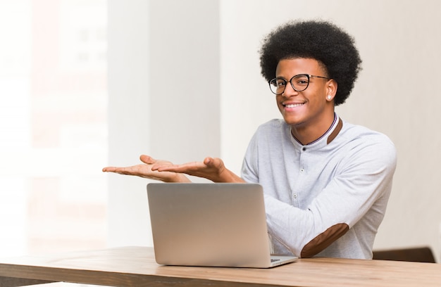 Hombre negro joven que usa su computadora portátil que lleva a cabo algo con la mano