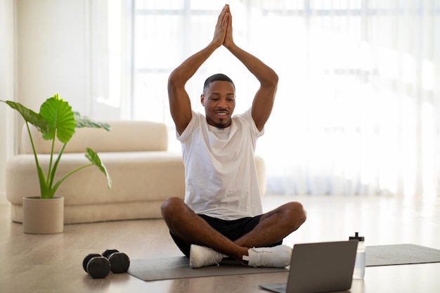 Hombre negro meditando en casa viendo videos en Internet