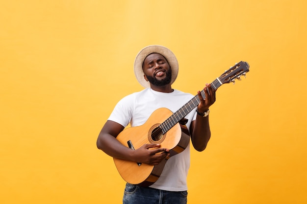 Hombre negro musculoso tocando la guitarra, vestido con jeans y camiseta blanca sin mangas.