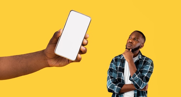 Hombre negro pensativo mirando una gran pantalla de teléfono inteligente vacía en blanco
