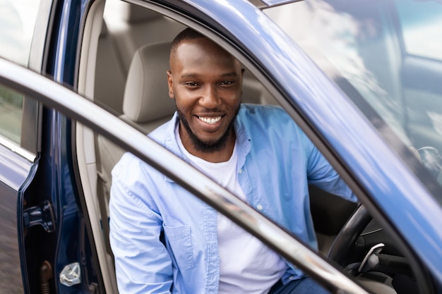 Hombre negro sonriente conduciendo un coche nuevo en la ciudad