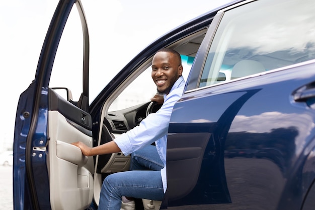 Hombre negro sonriente conduciendo un coche nuevo en la ciudad