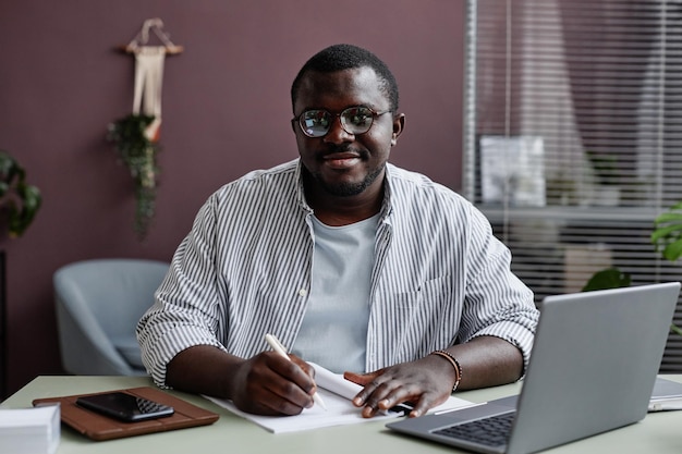 Hombre negro sonriente con gafas en el lugar de trabajo en la oficina