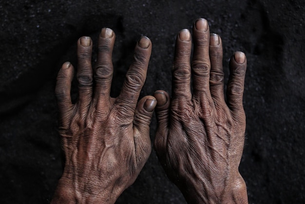 Hombre negro trabajador manos duras sobre fondo de suelo oscuro, primer plano