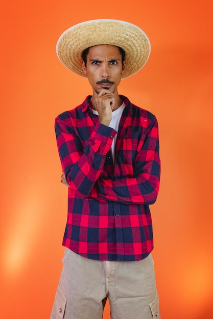 Hombre negro con traje de fiesta Junina aislado sobre fondo naranja Joven vistiendo ropa tradicional para el festival brasileño Festa Junina de junio