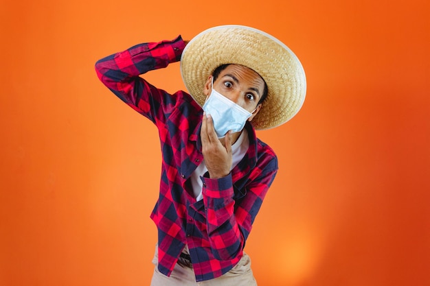 Hombre negro con traje de fiesta Junina con máscara pandémica aislado sobre fondo naranja Joven vestido con ropa tradicional para el festival brasileño Festa Junina de junio