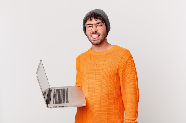 Hombre nerd con computadora sintiéndose disgustado e irritado, sacando la lengua, disgustando algo desagradable y asqueroso
