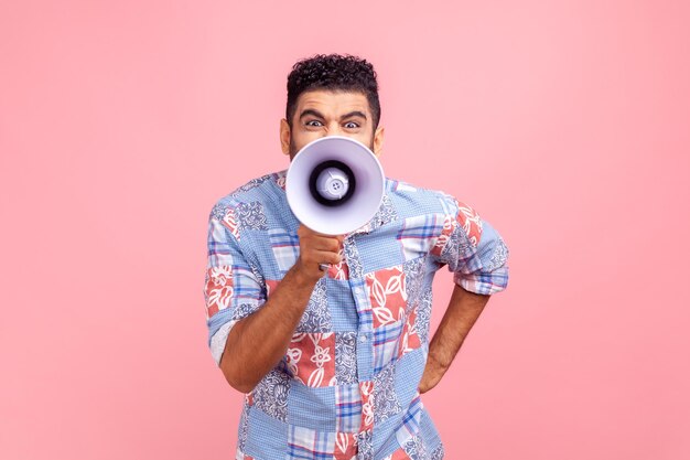 Hombre nervioso con barba en camisa de estilo casual gritando en megáfono haciendo anunciar protestando mirando a la cámara con expresión enojada Camisa de estudio interior aislada sobre fondo rosa