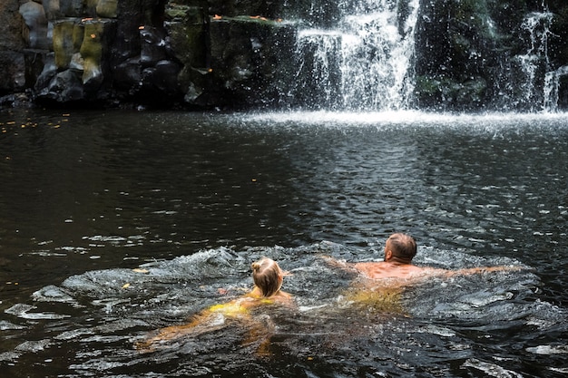 Foto un hombre y una niña están nadando en una cascada. gente en la cascada de la cueva. baños.