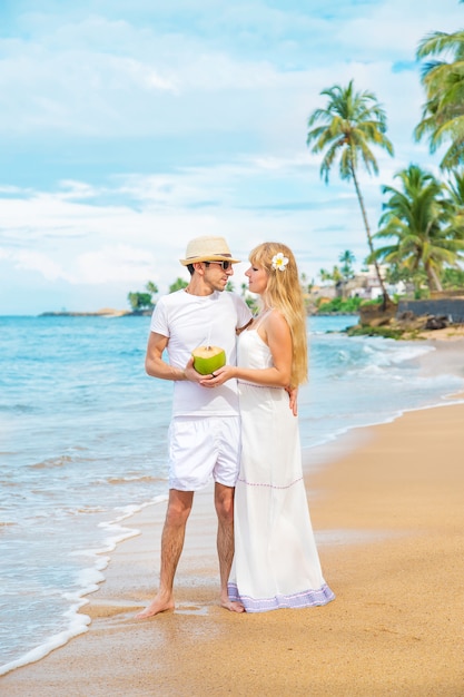 Un hombre y una niña en la playa beben coco.