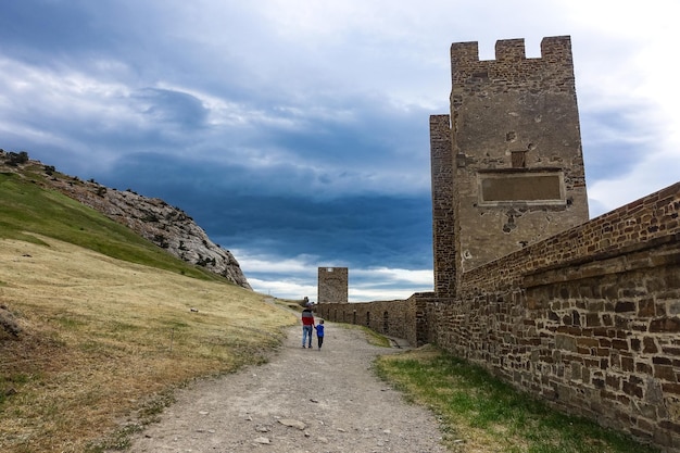 Un hombre con un niño en el contexto de una antigua fortaleza genovesa con un cielo tormentoso Sudak