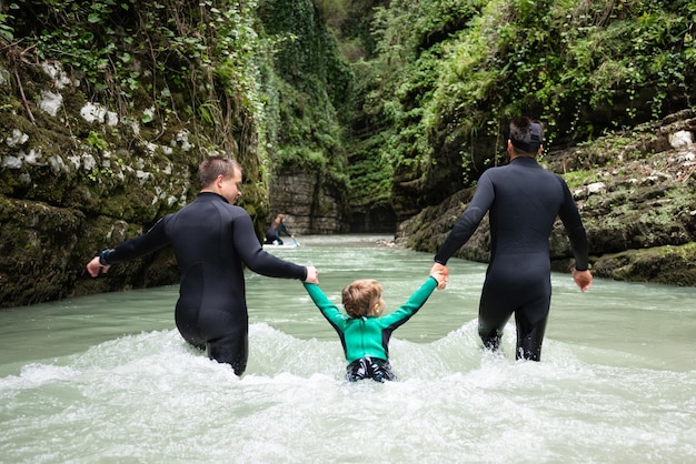 Un hombre con un niño en traje de neopreno en un cañón con un río