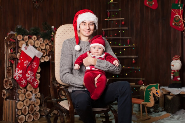 Un hombre con un niño vestido como Santa Claus en un sillón junto a una chimenea de madera en la víspera de Año Nuevo