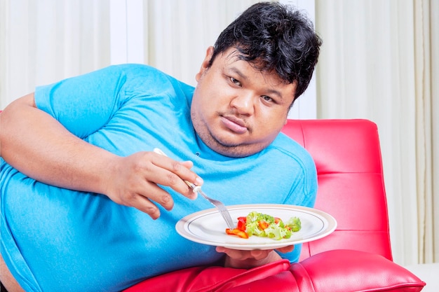 Hombre obeso que odia comer ensalada saludable en casa