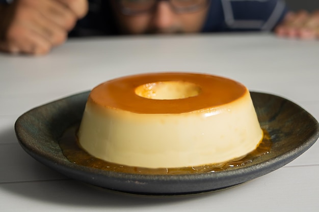 Un hombre observa un budín o un flan en un plato oscuro.